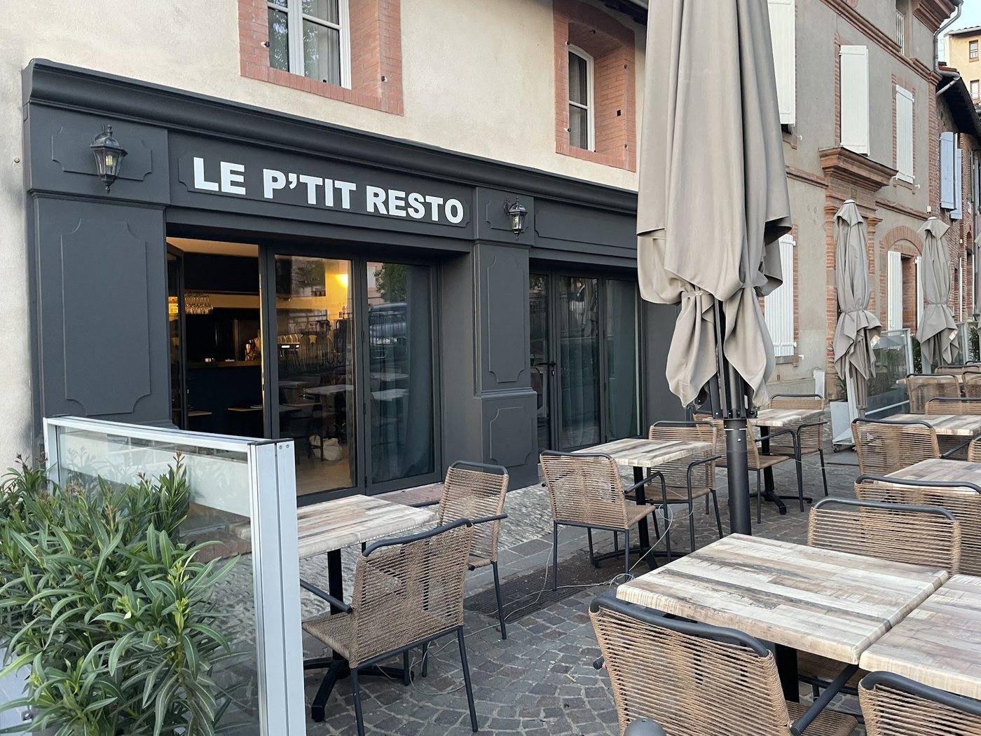 La devanture gris ardoise du P’tit Resto, enseigne en lettres blanches, ouverte sur la salle, et sa terrasse sur les pavés de la place du Château à Albi.