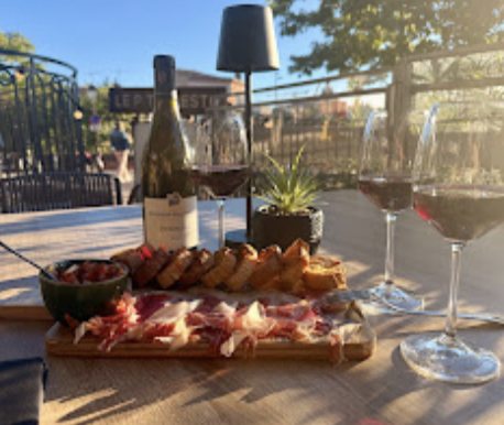 Planche de charcuterie et de pain grillé, deux verres de vin rouge, en terrasse au soleil couchant.