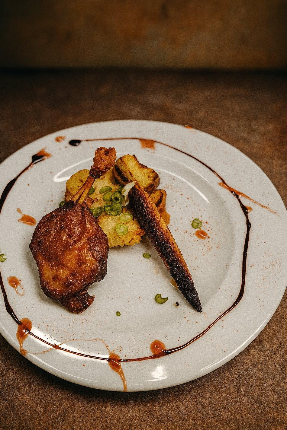 Assiette dressée : viande confite dorée, écrasé de pommes de terre aux cébettes, carotte rôtie et cordon de jus réduit.