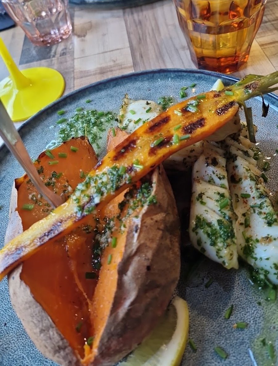 Patate douce ouverte, calamars grillés au persil et carotte rôtie sur une assiette bleue, verre de rosé posé à côté.